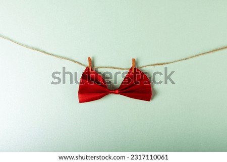 Close-up of red bowtie hanging with clothespins on clothesline against white background, copy space. Menswear, fashion, elegance concept.