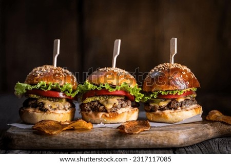 Three burger sliders placed on a wooden board in rustic atmosphere. Very tasty burgers with melted cheese, lettuce, tomato and sauce