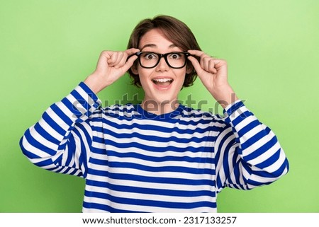 Photo of young astonished funky girl wear striped sailor shirt hold eyeglasses unexpected vision improvement isolated on green background
