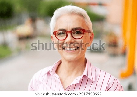 Portrait of smiling senior woman wearing red stylish eyeglasses looking at camera on the street. Successful business concept 
