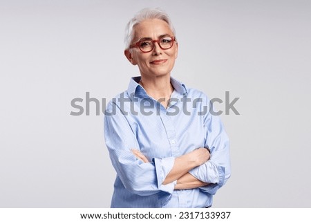 Portrait of confident senior businesswoman, manager, CEO holding arms crossed isolated on gray background, successful business. Attractive gray haired teacher wearing eyeglasses looking at camera 