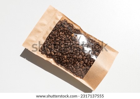 A brown kraft paper bag with a coffee bean lock for viewing with a highlighted shadow on a white background. Layout of the packaging template for food and essential goods. Royalty-Free Stock Photo #2317137555
