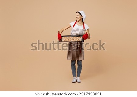 Full body young housewife housekeeper chef baker latin woman wear striped apron toque hat woman hold baking sheet with chocolate cookies look aside isolated on plain beige background Cook food concept Royalty-Free Stock Photo #2317138831