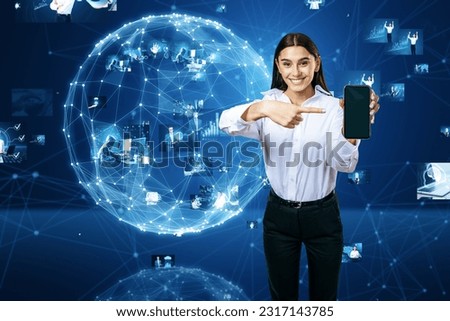 Connecting businesspeople, video conference concept. Attractive happy young european businesswoman pointing at cellphone with abstract blue globe with polygonal mesh and images on blurry background