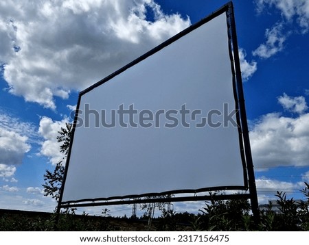 aluminum stage construction. large format white screen, tarpaulin, outdoor cinema in park. secured with drawstrings.  screening under sky is set up in park, black, clouds, blue sky, project, banner