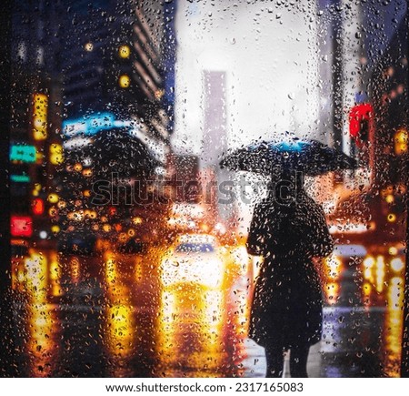 View through a glass window with raindrops on a blurred silhouette of a girl with umbrella walking on autumn rain , night street scene. focus on raindrops Royalty-Free Stock Photo #2317165083