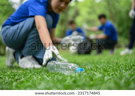 Close-up image of a beautiful and kind young Asian female volunteer collecting trash and a plastic bottle in the public park, helping her team clean up the park. Royalty-Free Stock Photo #2317174845