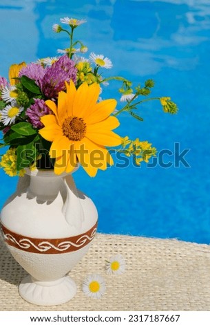 A bouquet of wild flowers in a small vase against the background of the pool. On a summer sunny day.