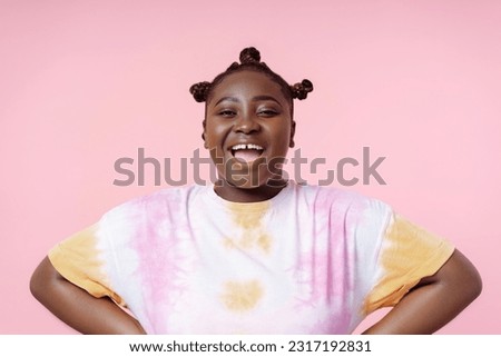 Smiling positive african woman wearing t shirt looking at camera isolated on pink background. Body positive female, summer concept