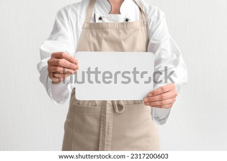 Female chef holding blank card on light background, closeup