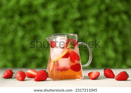 Jug of strawberry lemonade on white table outdoors