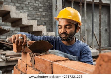 Happy Indian male construction worker constructing brick wall - hard working concept, manual labour Royalty-Free Stock Photo #2317221223