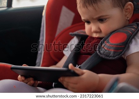 the child is sitting in a car seat, holding a mobile phone in his hands, watching cartoons on the phone, the child is playing on the phone, the entertainment of the child on the journey