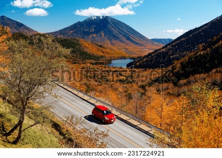 A car driving on the mountain highway at Konsei Pass with beautiful fall colors covering the hills and Yunoko Lake located at the foot of Mount Nantai in Yumoto, Nikko National Park, Tochigi, Japan