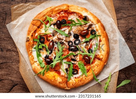 Pizza with salami sausage, mozzarella cheese, mushrooms, black olives, spicy tomato sauce and arugula, rustic wooden table background, top view