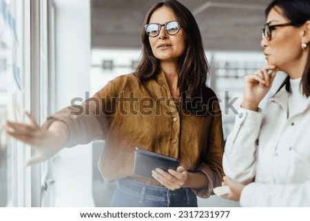 Mature business woman brainstorming with her colleague in an office. Female professionals discussing business ideas using sticky notes. Royalty-Free Stock Photo #2317231977
