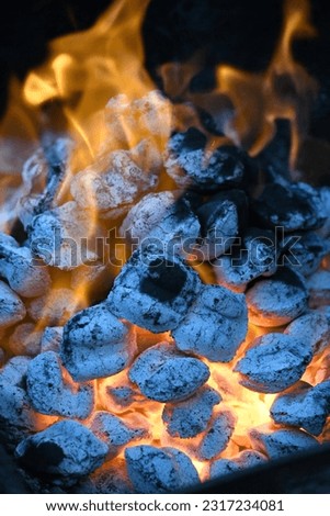 Orange flames flair high in this image of a grill, with white hot charcoal briquettes that are nearly ready to cook food. The picture is outlined by dark black making the flames look dramatic.
