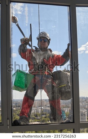 A blurry view through a dirty window of a window washer. Rope access. An alpinist washes windows Royalty-Free Stock Photo #2317256263