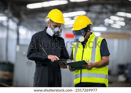 Two officers wearing gas masks, holding tablet and book, inspect the chemical spill site in an industrial warehouse to assess the damage, wearing gas masks, inspecting and evaluating toxicity of leak. Royalty-Free Stock Photo #2317269977