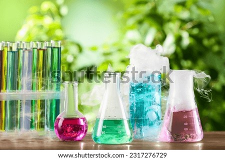 Laboratory glassware and test tubes with colorful liquids on wooden table outdoors. Chemical reaction