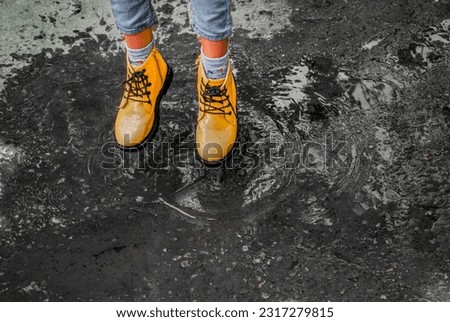 Waterproof children's shoes in a puddle. Yellow fashion rubber boots with tractor soles. Rainy weather shoe concept. Splashes fly in all directions.
