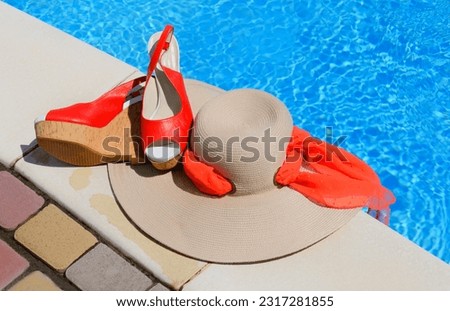 Women's hat, sandals and starfish next to the pool. Red beautiful sandals and straw on a background of blue water