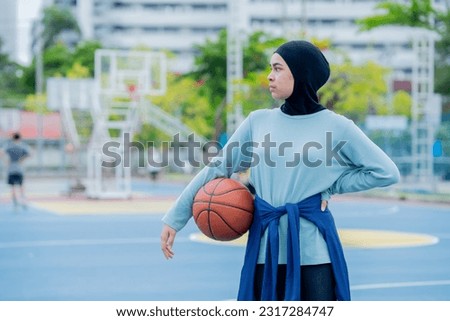 Young asian muslim girl teen wearing hijab going to play basketball on the outdoor court in the morning with determination, Muslim sport concept.