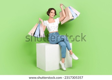 Full length photo of sweet cheerful woman dressed white blouse siting cube rising bargains isolated green color background