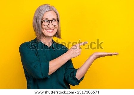 Photo of pretty positive aged lady look direct finger arm hold empty space isolated on yellow color background