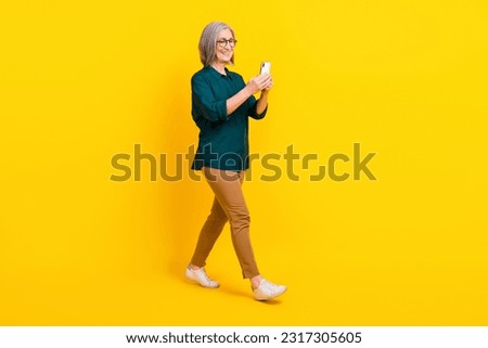 Full size profile portrait of positive lady use smart phone walking isolated on yellow color background
