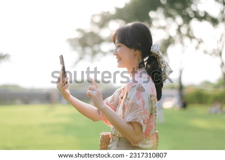 Portrait of young asian woman traveler with weaving basket, mobile phone on green public park background. Journey trip lifestyle, world travel explorer or Asia summer tourism concept.