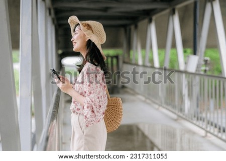 asian young woman traveler with weaving basket using mobile phone and standing on overpass. Journey trip lifestyle, world travel explorer or Asia summer tourism concept.