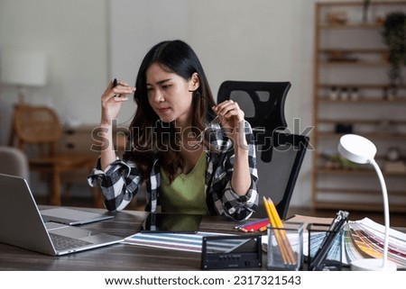 Serious and focused female graphic designer sitting at her desk, surrounded by sketches and drawings