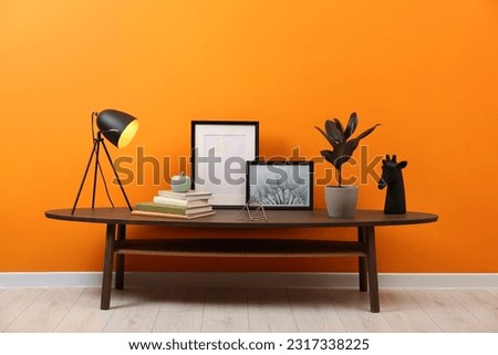 Wooden coffee table with different decor near orange wall indoors. Stylish interior design