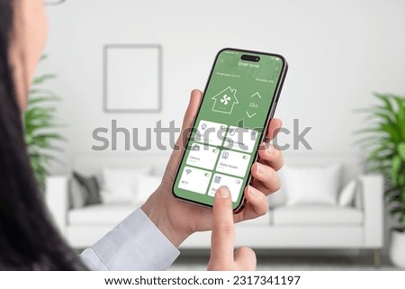 Woman use smart home app on smart phone. Living room interior in background. Home automation concept