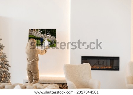 Modern Home Interior And Domestic Decor. Smiling young woman hanging painting, putting photo picture frame on the wall. Casual lady taking care of coziness in her new stylish apartment, profile