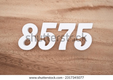 White number 8575 on a brown and light brown wooden background.