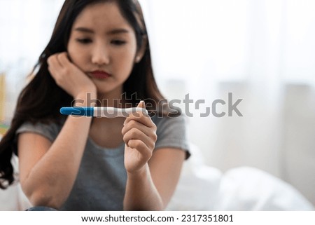 Asian woman sitting bed feeling disappointed when see the pregnancy test result. Woman feels worry and not ready to be a mother. Man feeling stress about the future kid holding head. Royalty-Free Stock Photo #2317351801