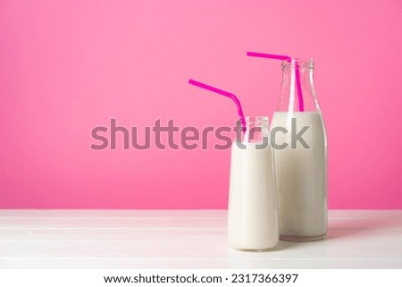 Two glass bottles of milk or milkshake against pink background