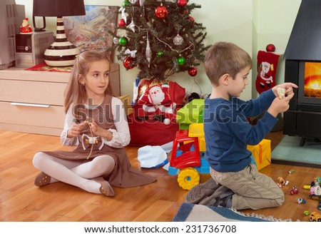 Brother and sister opening Christmas gifts in front of Christmas tree.