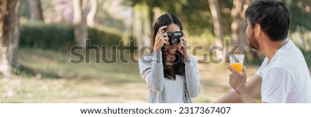 Happy asian couple travel. Woman taking photo of his boyfriend picnic time in park holidays vacation