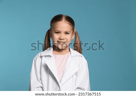 Portrait of little girl in medical uniform on light blue background