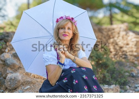 Beautiful woman in typical Austrian costume holds an umbrella on a sunny spring day. Royalty-Free Stock Photo #2317371325