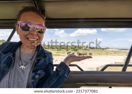 Forced perspective composition of a woman in a safari vehicle pretends to hold a herd of elephants Royalty-Free Stock Photo #2317377081