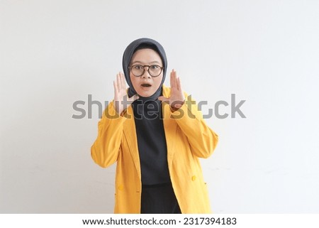 beautiful young Asian Muslim woman, wearing glasses and yellow blazer with shocked expression isolated on white background.