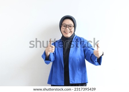 beautiful young Asian Muslim woman, wearing glasses and blue blazer with hand gesture of approval or OK isolated white background.