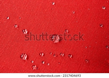 Clear water drops on red canvas, soft focus close up