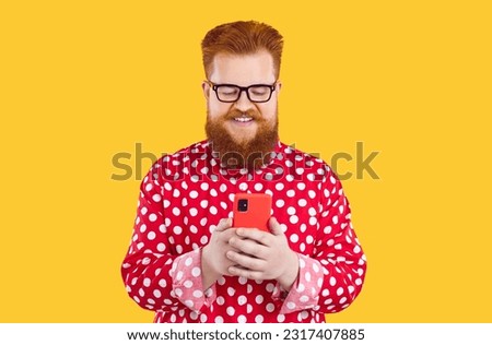 Happy bearded fat man uses his mobile phone for online shopping, chatting, using mobile applications and browsing social networks. Cheerful bearded chubby guy with smartphone on orange background.