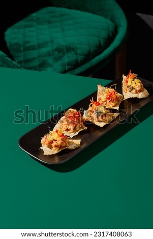 Salmon and mango tartare on wheat pancakes, an Asian cuisine delight. Served on a black plate in a modern minimalist Asian restaurant, with a green chair in the background.