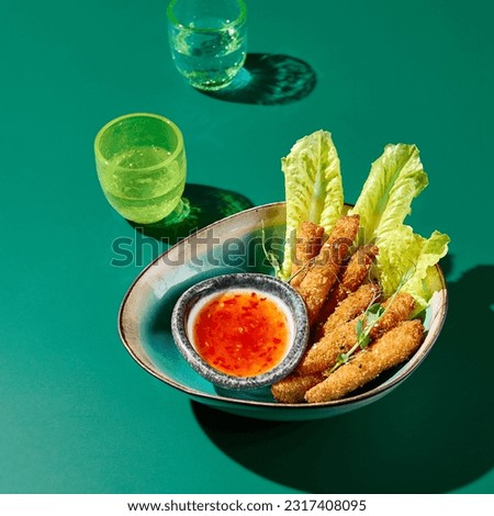 Asian snack - Chicken tempura strips with sweet chili sauce in a ceramic bowl on a green background with colored glasses. Bright light, Hard shadows. Menu of an Asian restaurant.